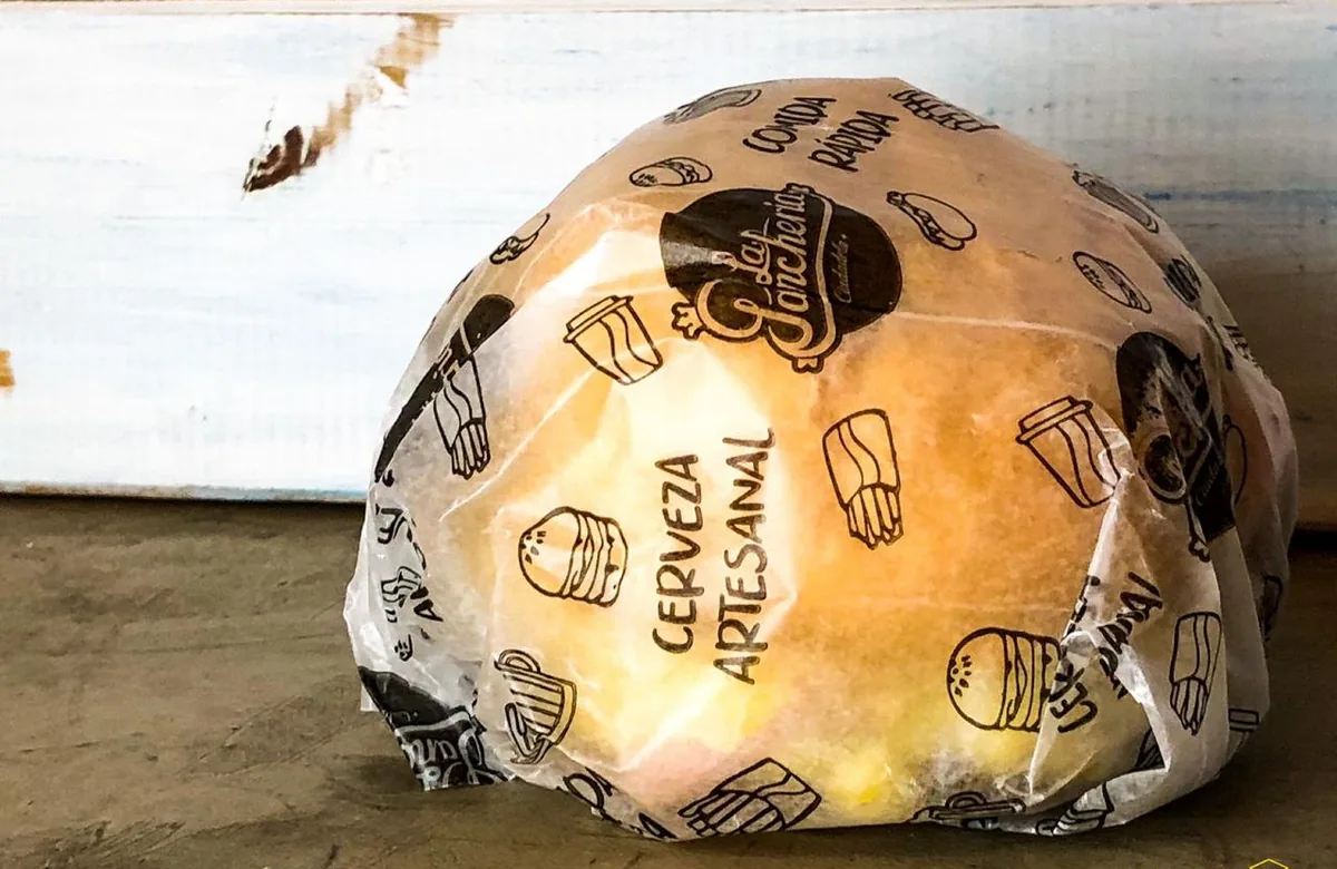 Hamburguesa envuelta en papel parafinado impreso con el logo del local